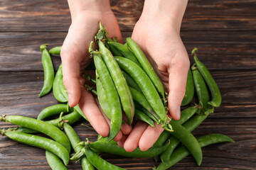 Woman with fresh green peas at wooden table, closeup