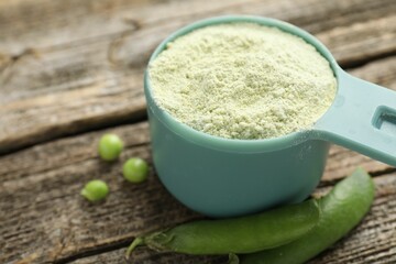 Protein powder in measuring spoon and fresh green peas on wooden table, closeup