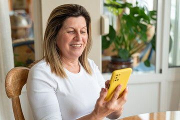 Smiling elderly female engaging with smartphone, connecting through digital communication at home