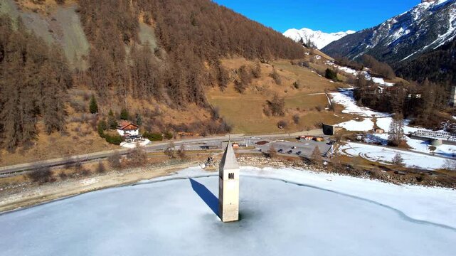 Church tower of Reschen - Vinschgau, South Tyrol - landing panoramic aerial view around the tower on the frozen lake
