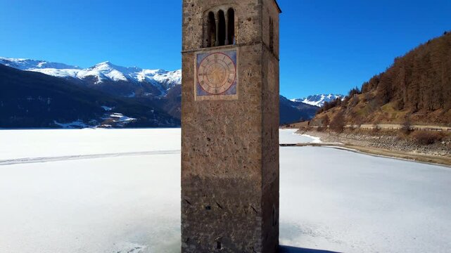 Church tower of Reschen - Vinschgau, South Tyrol - rising climbing aerial photograph of the tower with a view of the frozen Lake Rechen