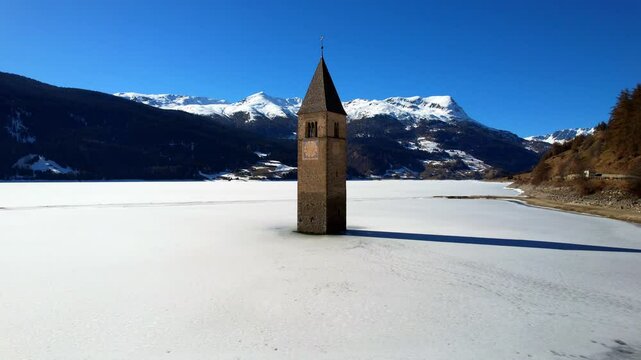 Church tower of Reschen - Vinschgau, South Tyrol - rising spectacular aerial view of the frozen lake