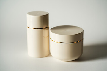 Two CreamColored Cosmetic Containers with Gold Accents on a Neutral Surface, Minimalist Aesthetic