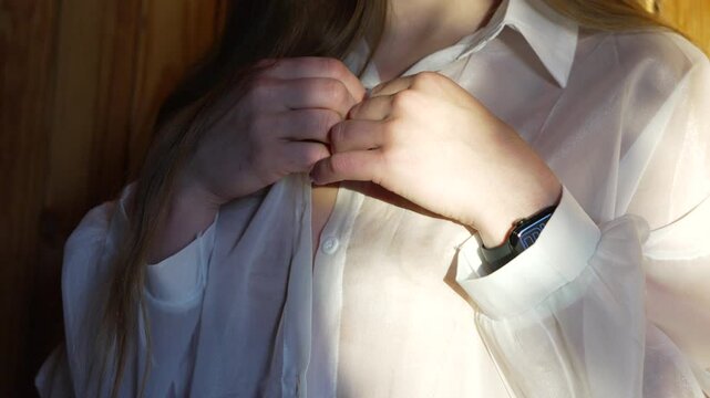 Hands Buttoning Shirt Woman adjusting sheer white blouse indoors
