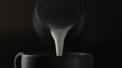 Slow motion pour steamed milk into espresso in black cup closeup - Powered by Adobe