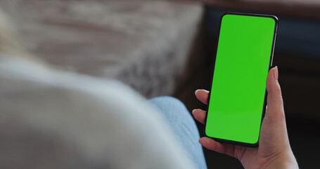young woman sitting in a chair with smartphone with green screen