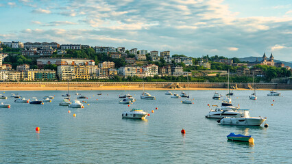 Beautiful sunset over La Concha Bay with boats anchored in the calm water, San Sebastian, Basque...
