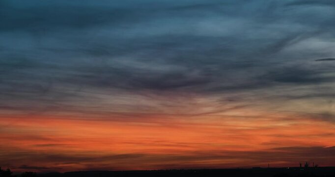 Timelapse of beautiful nightfall cloudscape scenery with beautiful bright orange glow in the sky slowly receding and clouds getting dark blue above flat countryside