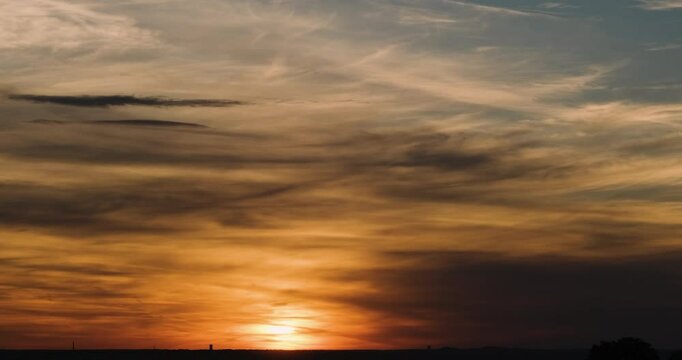 Glowing Sun Sinking Behind a Low Flat Horizon Lighting Thin Slow Moving Orange Clouds in an Evening Sky 4K Time Lapse Capturing Warm Sunset Radiance and Gentle Cloud Drift Over Open Landscape