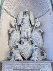 A low-angle, full-frame shot focuses on an imposing neoclassical white marble statue of a stylized...