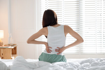 Woman stretching on bed with soft mattress at home, back view