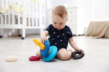 Cute little baby playing with toy pyramid in room