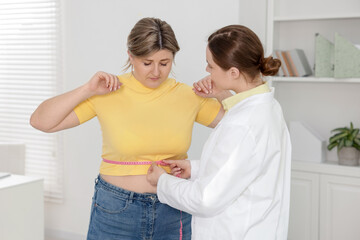 Weight loss. Nutritionist measuring overweight woman's waist with tape in clinic