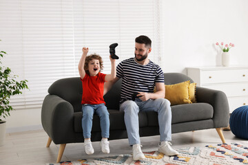 Happy father and his son playing with game controllers together on sofa at home
