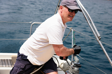 Mature man sailing in Costa Brava, adjusting sails on sailboat winch