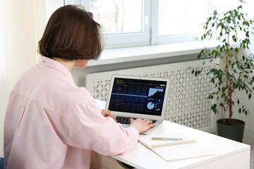 Stock exchange. Woman analysing financial market on laptop at white table indoors