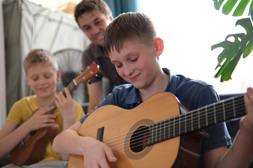Smiling father teaches his sons to play guitar at home, family music lesson