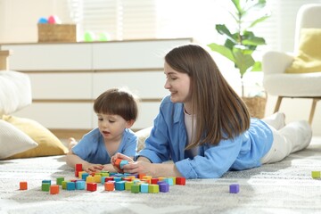Mother and son playing with colorful cubes at home. Space for text