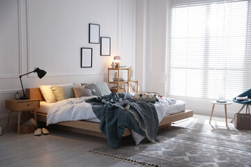 Cozy bed with soft linens, nightstand and lamp in stylish room. Home textile
