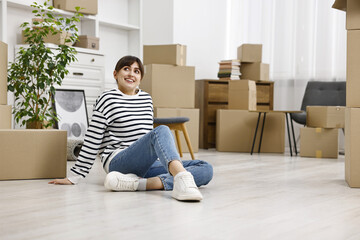 Moving day. Happy woman resting on floor and cardboard boxes in her new home