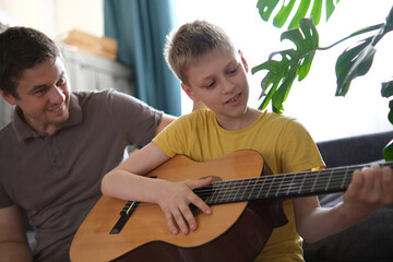Father teaching his son to play guitar at home, family bonding