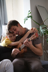 Father teaching son ukulele, smiling and bonding warmly at home