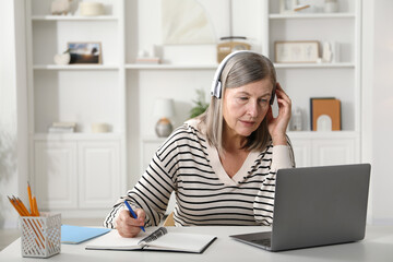 Woman learning online using laptop and taking notes at table indoors. Self-study