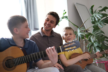 Happy father and sons playing guitars together and smiling at home
