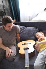 Happy father and his son sitting on the sofa after guitar lesson at home