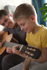 Father teaching his son to play guitar at home, family bonding