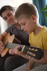 Father teaching his son to play guitar at home, family bonding