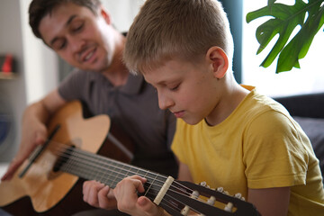 Father teaching his son to play guitar at home, family bonding