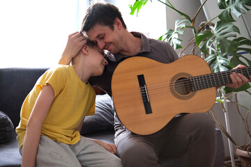 Father and son hugging warmly while playing guitar at home, enjoying music
