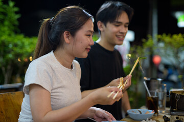 Young Asian couple eating Thai Food BBQ Grill Mu Kratha at night