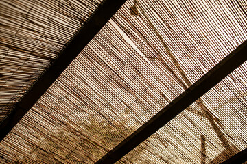 Wooden beams supporting a reed screen creating a pattern of light and shadow