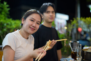 Young Asian couple eating Thai Food BBQ Grill Mu Kratha at night