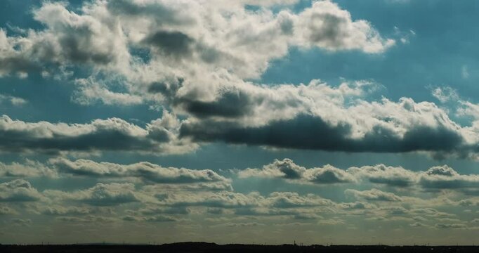 Timelapse of white and grey cumulus clouds rolling in the blue sky like waves creating dreamy atmosphere as rays of sunlight shine through