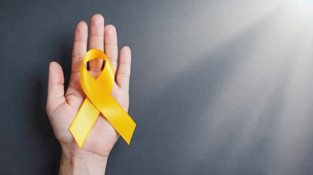 Hand holding yellow sarcoma awareness ribbon, gray background.