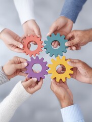 Multiple hands of varying ethnicities hold colorful gears, showcasing unity and cooperation. The soft-focus background enhances the vibrant colors and the connection among participants.