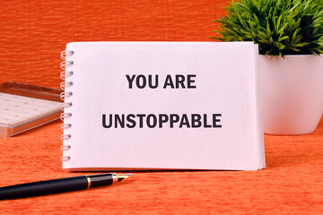 Concept text YOU ARE UNSTOPPABLE on a spiral notebook on an orange background