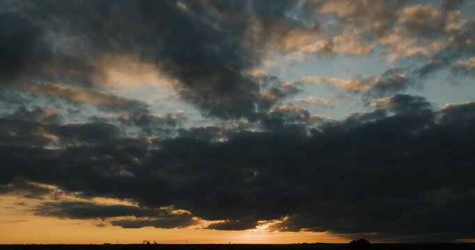 Timelapse of cloudy sunset sky above flat landscape capturing the sun emerging from behind a dark cloud while creating an asterisk effect and descending below horizon as the scene is getting darker