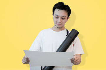 young asian man reading documents or project paper on isolated yellow background
