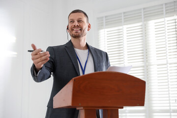 Man giving public speech with microphone at lectern indoors