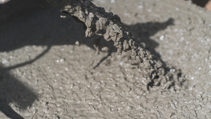 Close-up of wet concrete being poured, showing rich texture and motion in construction work. Perfect for themes of raw material, industrial process, and real-world building scenes.
