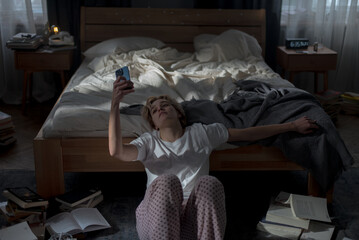 Pensive young woman using smartphone sitting on floor
