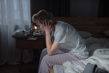 Blonde young woman cries from desperation sitting on bed