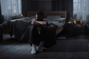 Pensive African American guy calms down with self hugging sitting on room floor