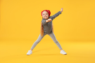 Cute little girl dancing on orange background