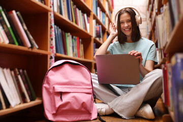 Student with laptop and backpack between shelves in library