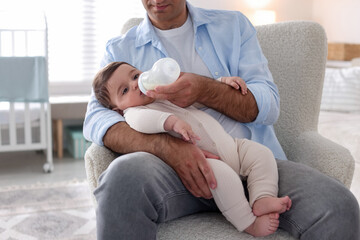 Fototapeta premium Father feeding his little baby with bottle on armchair at home, closeup